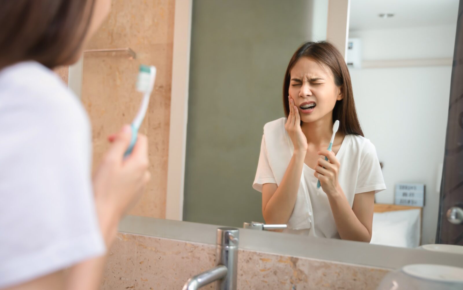young-asian-woman-brushing-teeth-with-sensitive-teeth-and-hands-touch-the-cheeks--1600x1003